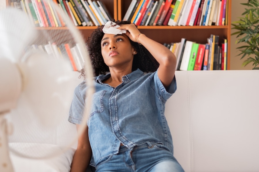 Why is My AC Blowing Out Warm Air?  Black woman sweating and trying to refresh at home.