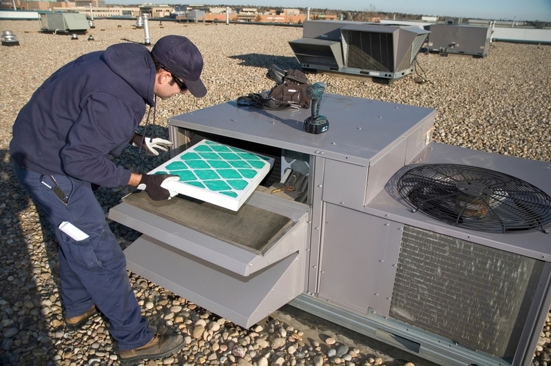 Worker changing a roof top air exhange units filter.