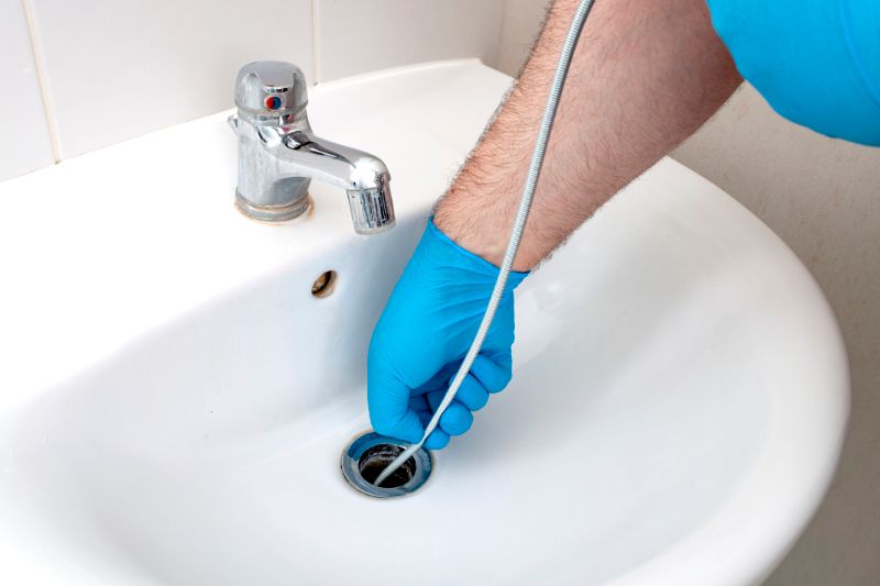 Image of someone snaking a drain with blue latex gloves. Why Do My Drains Keep Clogging?