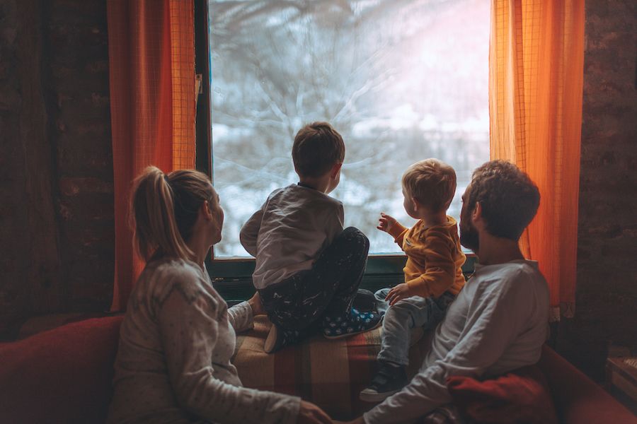 7 Tips to Conserve Heat Inside Your Home This Winter. Image shows family sitting on couch and looking out window at snow.