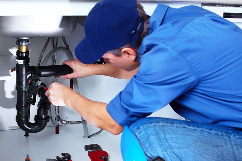 5 Plumbing Tips to Save Money During a PNW Summer. Photo of a plumber working on a kitchen sink.